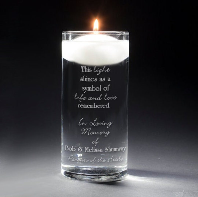 May include: A clear glass cylinder vase with a floating candle and an engraved message: "This light shines as a symbol of life and love remembered. In Loving Memory of Bob & Melissa Shumway Parents of the Bride"
