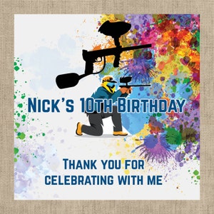 May include: A colorful birthday party favor tag with a paintball player graphic. The tag says "Nick's 10th Birthday" and "Thank you for celebrating with me".