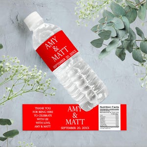 May include: A clear plastic water bottle with a red label that reads "AMY & MATT SEPTEMBER 20, 20XX." A second red label reads "THANK YOU FOR BEING HERE TO CELEBRATE WITH US WITH LOVE AMY & MATT." The bottle is surrounded by greenery.