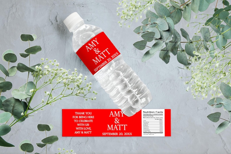 May include: A clear plastic water bottle with a red label that reads "AMY & MATT SEPTEMBER 20, 20XX." A second red label reads "THANK YOU FOR BEING HERE TO CELEBRATE WITH US WITH LOVE AMY & MATT." The bottle is surrounded by greenery.