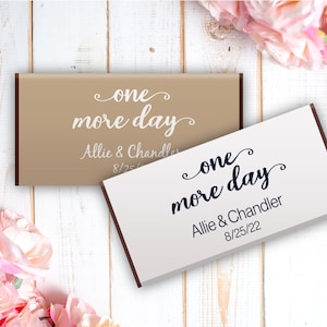 May include: Two chocolate bar wrappers with the text "one more day" in a cursive font. The wrappers are brown and white with the names Allie & Chandler and the date 8/25/22 printed on them.