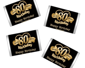 May include: Four black and silver chocolate bar wrappers with gold foil accents. The wrappers feature the text "1939 80th 2019 Birthday Happy Birthday Jessical".