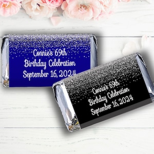May include: Two chocolate bar wrappers with a silver glitter design. The top wrapper is blue with white text that reads "Connie's 69th Birthday Celebration September 16, 2024". The bottom wrapper is black with white text that reads "Connie's 69th Birthday Celebration September 16, 2024".