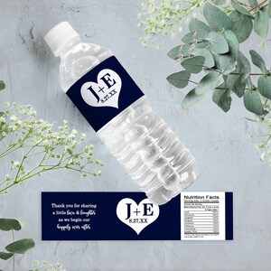 Op de afbeelding: Donkerblauwe bruiloftwaterfleslabels met witte tekst en een hartvormig ontwerp. De labels zeggen "J+E 8.27.XX" en "Bedankt voor het delen van een beetje gezicht en gelach terwijl we beginnen aan ons geluk voor altijd".