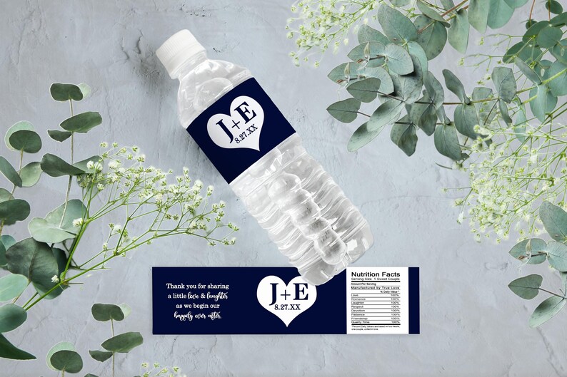 Op de afbeelding: Donkerblauwe bruiloftwaterfleslabels met witte tekst en een hartvormig ontwerp. De labels zeggen "J+E 8.27.XX" en "Bedankt voor het delen van een beetje gezicht en gelach terwijl we beginnen aan ons geluk voor altijd".