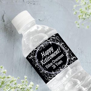 May include: Black and white water bottle label with a decorative border and the text "Happy Retirement! Eldon Overstreet 28 Years".