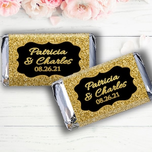May include: Two gold glitter chocolate bar wrappers with black labels. The labels have the text "Patricia & Charles" and the date "08.26.21".