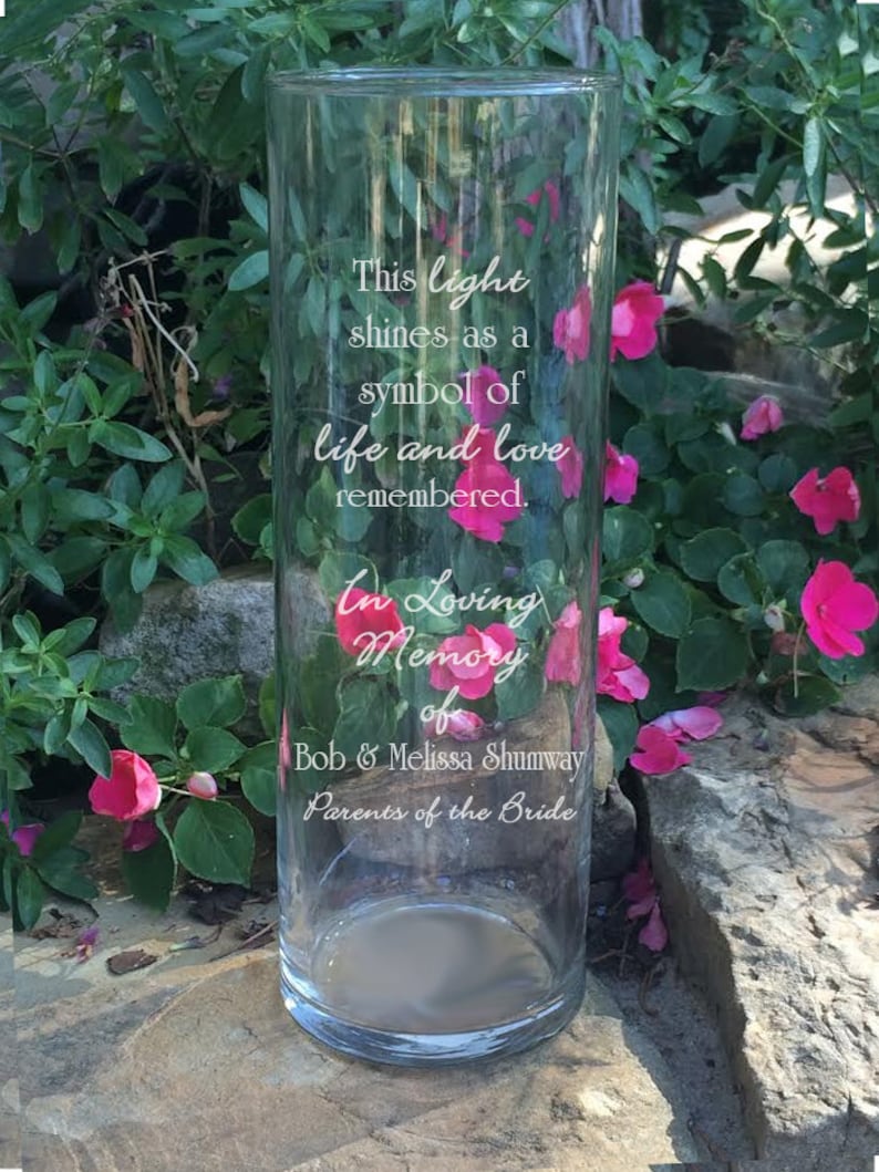 May include: A clear glass vase with an inscription that reads "This light shines as a symbol of life and love remembered. In Loving Memory of Bob & Melissa Shumway Parents of the Bride".