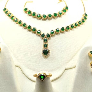 Op de afbeelding: Een gouden sieradenset met groene hartvormige stenen. De set bevat een ketting, een armband, een ring en een paar oorbellen.