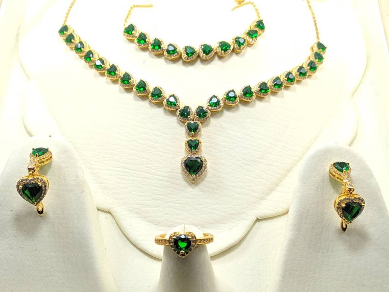 Op de afbeelding: Een gouden sieradenset met groene hartvormige stenen. De set bevat een ketting, een armband, een ring en een paar oorbellen.