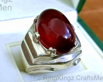 May include: A silver ring with a large, oval-shaped, red gemstone. The ring has a detailed, textured design.