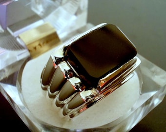 May include: A silver ring with a black onyx stone set in a square shape. The ring has a textured band.