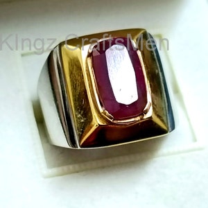 Könnte beinhalten: Ein Silber- und Goldring mit einem großen, ovalen, roten Edelstein, der in der Mitte eingesetzt ist.