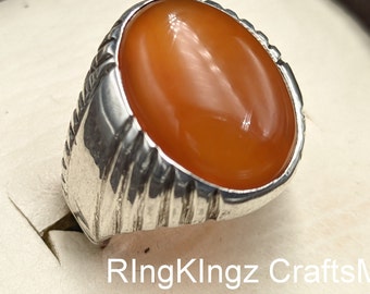 May include: A silver ring with an orange carnelian gemstone. The ring has a textured band.