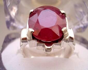 May include: A silver ring with a large, faceted, red ruby gemstone.