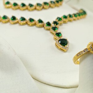 Op de afbeelding: Een gouden ketting- en ringset met groene hartvormige stenen en heldere zirkonia-accenten.