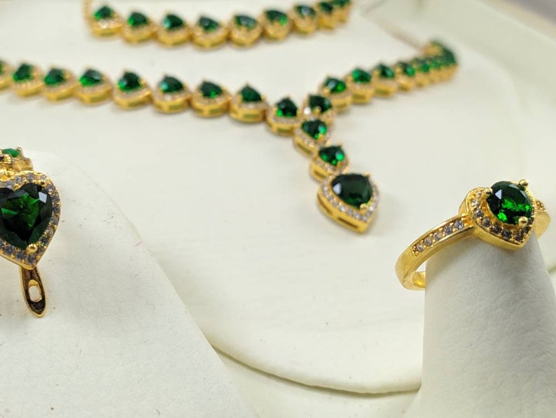 Op de afbeelding: Een gouden ketting- en ringset met groene hartvormige stenen en heldere zirkonia-accenten.