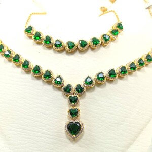 Op de afbeelding: Een gouden ketting- en armbandset met groene hartvormige stenen. De ketting heeft een hanger met een grotere hartvormige steen.