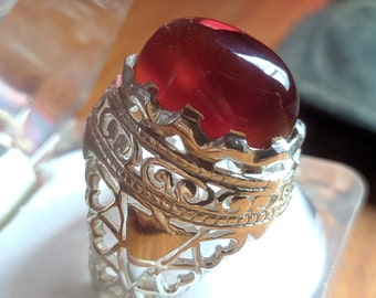 May include: A silver ring with an ornate design and a large, red gemstone.