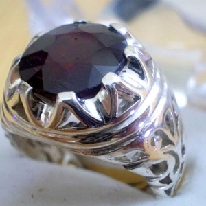 May include: A silver ring with an ornate design and a large, dark red gemstone.