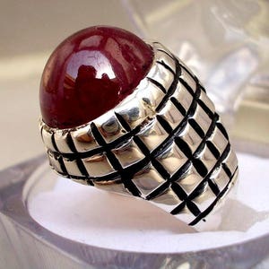Puede incluir: Un anillo de plata con una gran piedra preciosa de color rojo oscuro engastada en un patrón geométrico.