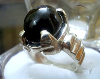 May include: A silver ring with a large, black gemstone set in a claw setting. The band of the ring is textured and has a decorative design.