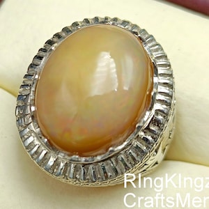 May include: A silver ring featuring a large, oval-shaped, iridescent opal gemstone. The ring has a detailed, textured band.