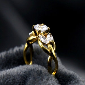 Op de afbeelding: Een gouden ring met drie heldere zirkonia-stenen. De ring heeft een gedraaid bandontwerp.