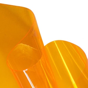 Puede incluir: Un rollo de lámina de plástico transparente naranja. La lámina es translúcida y tiene un ligero brillo.