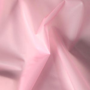 May include: A close-up of a pale pink fabric, showing folds and subtle highlights. The material has a smooth, possibly silky texture, with a gentle sheen. Light creates shadows and depth across the surface.