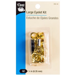 Puede incluir: Un paquete de ojales grandes de color dorado en un contenedor de plástico transparente. El paquete está etiquetado como "Dritz Large Eyelet Kit" y "Estuche de Ojales Grandes". El tamaño de los ojales es de 1/4 de pulgada (6,35 mm).