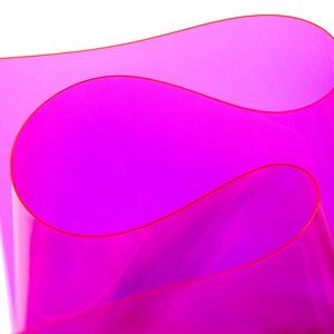 Puede incluir: Una lámina de plástico transparente de color rosa brillante doblada sobre sí misma, creando una forma curva.