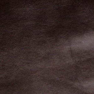 May include: Close-up of a dark brown leather texture. The leather has a smooth, slightly grainy surface.