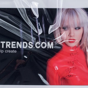 May include: A black and red business card with the text "MJTRENDS.COM" and the phrase "we help create". A woman with blonde hair and red lipstick is in the background wearing a red latex outfit.