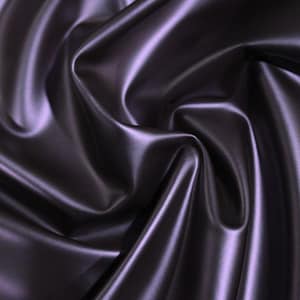 May include: Close-up of a smooth, silky fabric in a deep purple hue. The fabric is draped and folded, showcasing its luxurious texture.