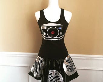 May include: A black tank top and skirt with a silver design of a robot face. The robot face has a red eye and a silver panel with a blue button.