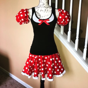 May include: A red and white polka dot dress with a black tank top and puff sleeves. The dress has a white lace trim.