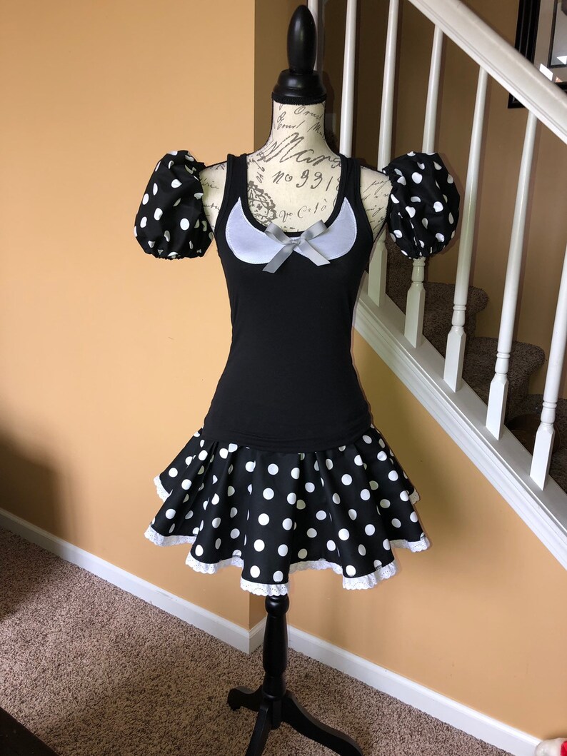 May include: A black and white polka dot dress with a white lace trim. The dress has a scoop neck and short sleeves with puffed shoulders. The dress is on a mannequin.