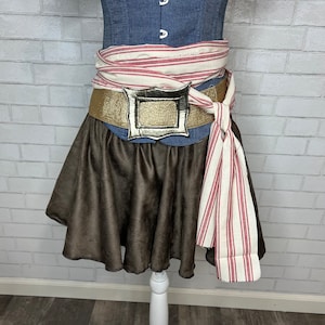 May include: A brown skirt with a gold belt and a silver buckle. The belt is tied with a white and red striped fabric.