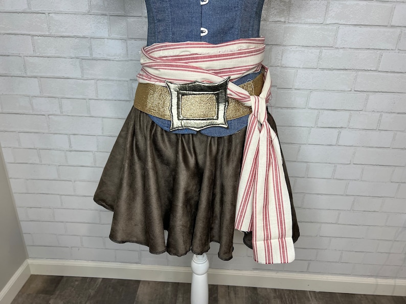 May include: A brown skirt with a gold belt and a silver buckle. The belt is tied with a white and red striped fabric.