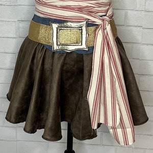 May include: A brown suede skirt with a ruffled hem. A gold belt with a silver buckle is worn over a denim skirt. A white and red striped fabric sash is tied around the waist.