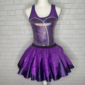 May include: Purple and silver sequined dress with a layered skirt. The top of the dress is a sleeveless bodice with a scoop neck.