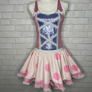 May include: A pink and white dress with a white top and a pink and white polka dot skirt. The top has a blue and white sequined design and pink bows on the straps. The skirt has a white lace trim.