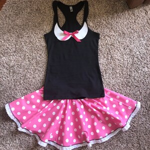 May include: A black tank top with a white collar and a pink bow. The tank top is paired with a pink skirt with white polka dots and a white lace trim.