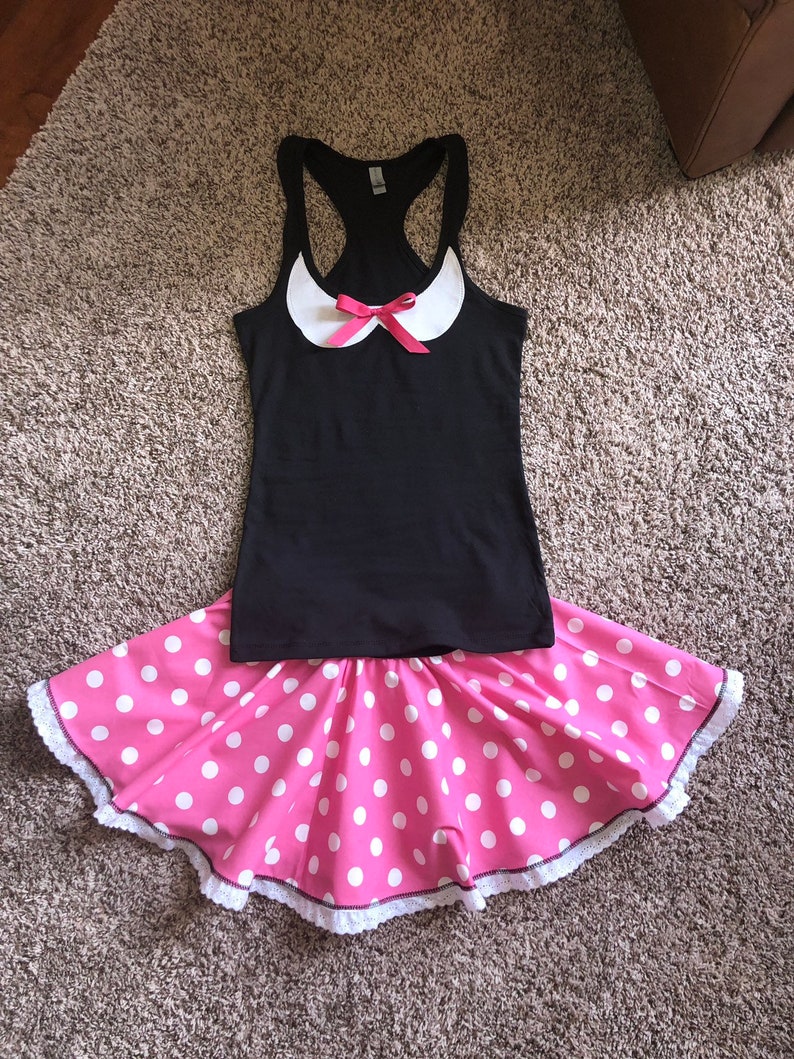 May include: A black tank top with a white collar and a pink bow. The tank top is paired with a pink skirt with white polka dots and a white lace trim.