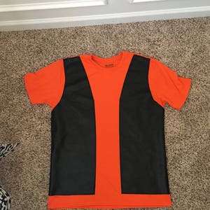 May include: Orange t-shirt with a black vest design printed on the front. The shirt has a crew neck and short sleeves. The brand name "Gildan" is printed on the tag.