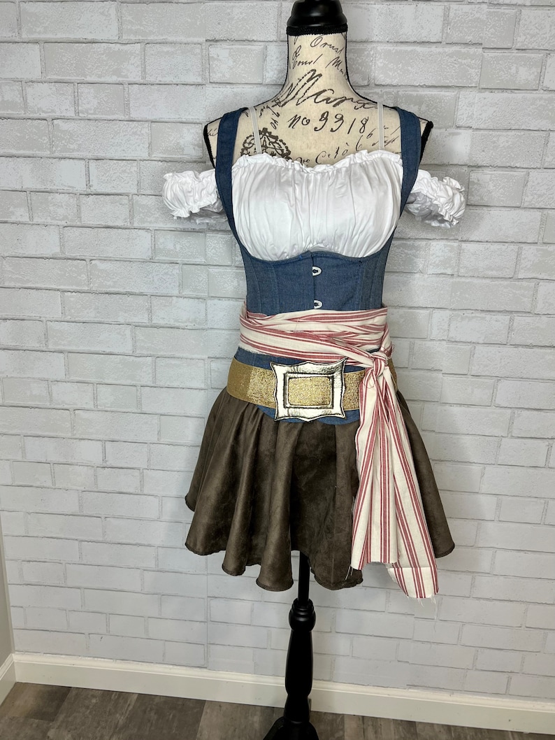 May include: A blue denim corset with a white peasant top and brown skirt. A red and white striped sash is tied around the waist with a gold buckle.