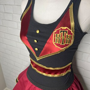 K&ouml;nnte beinhalten: Ein schwarzes und rotes Kleid mit goldenen Verzierungen. Das Kleid hat ein "Grand Floridian"-Logo auf der Vorderseite.