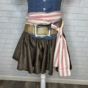 May include: A brown skirt with a gold belt and a silver buckle. The belt is tied with a white and red striped fabric.