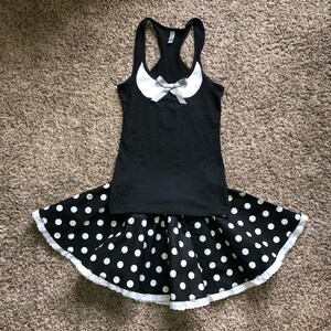 May include: A black tank top with a white collar and a white bow. The tank top is paired with a black and white polka dot skirt with a white lace trim.